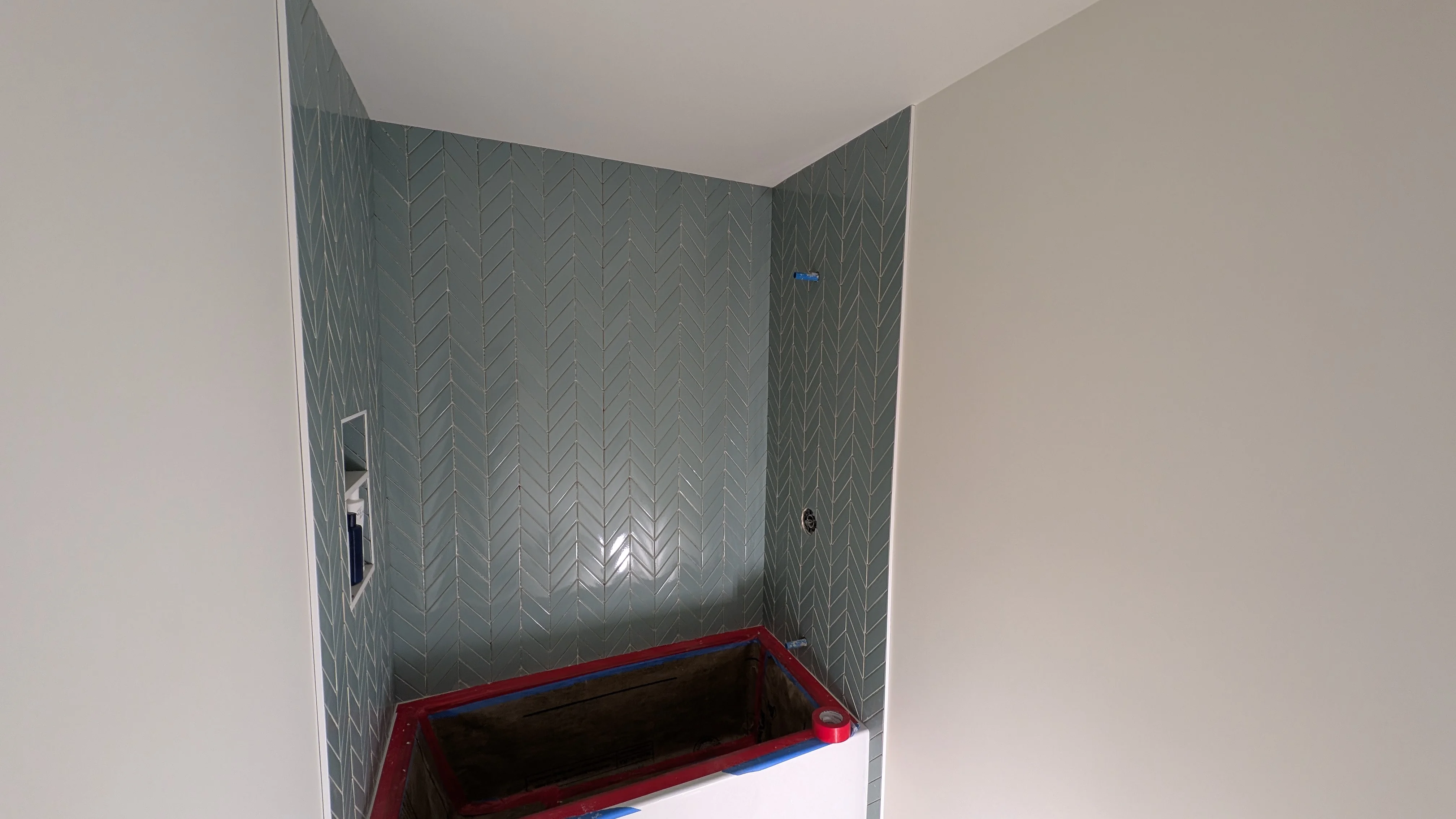 Gray herringbone tile shower enclosure with three tiled walls and white ceiling