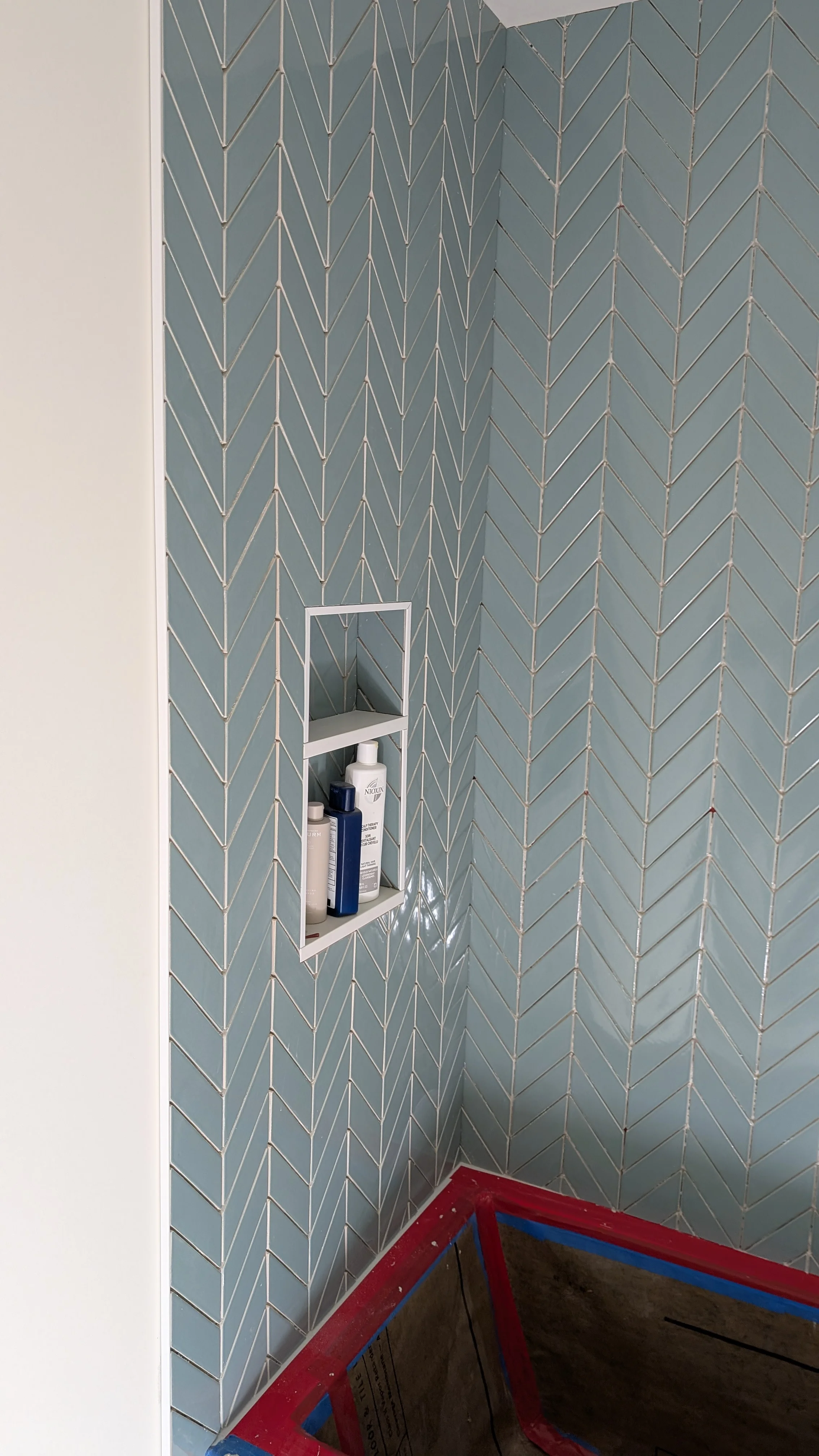 Blue herringbone tile shower wall with white recessed niche holding bathroom products