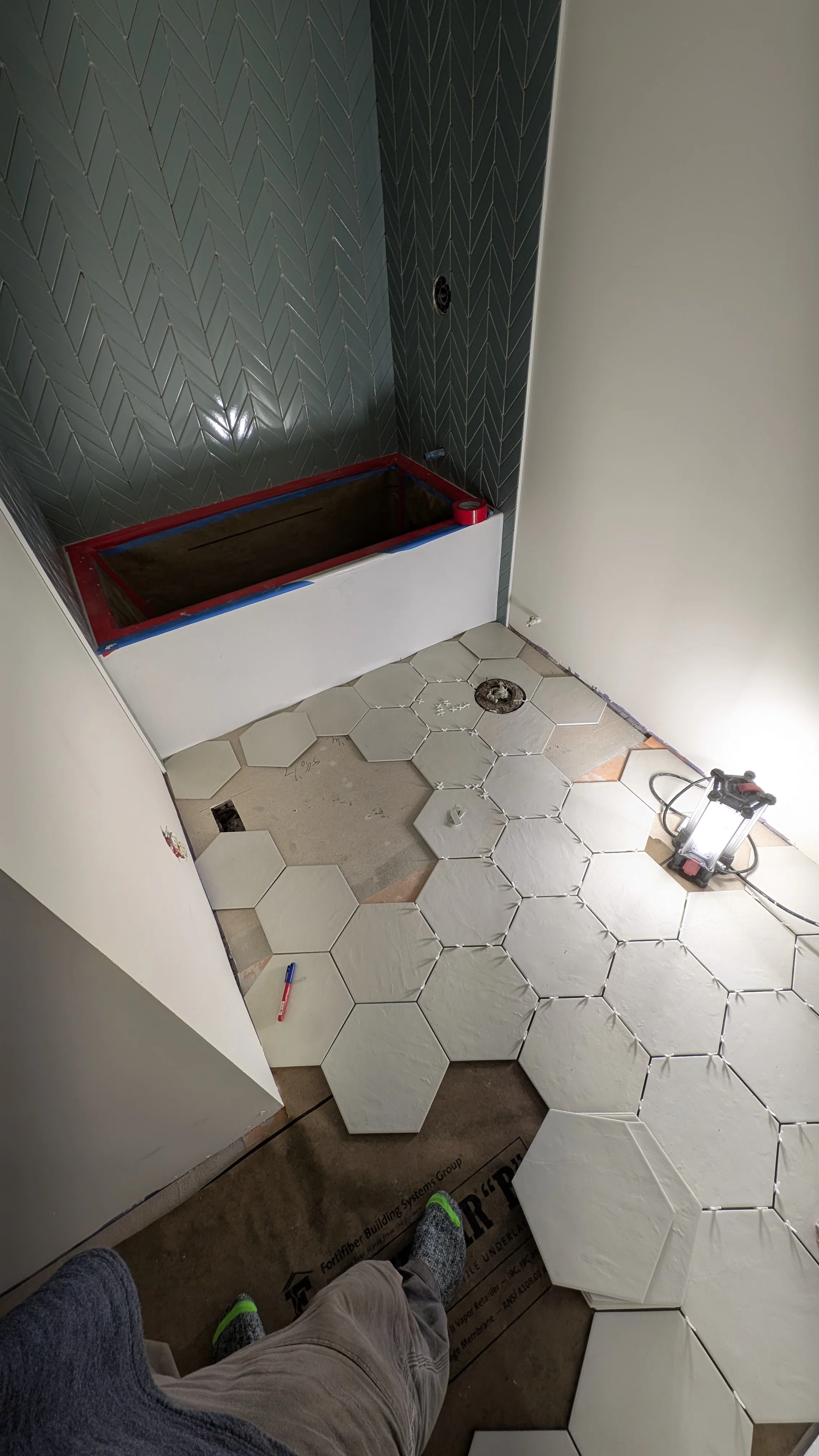Bathroom under renovation with hexagonal floor tiles and herringbone wall tile pattern