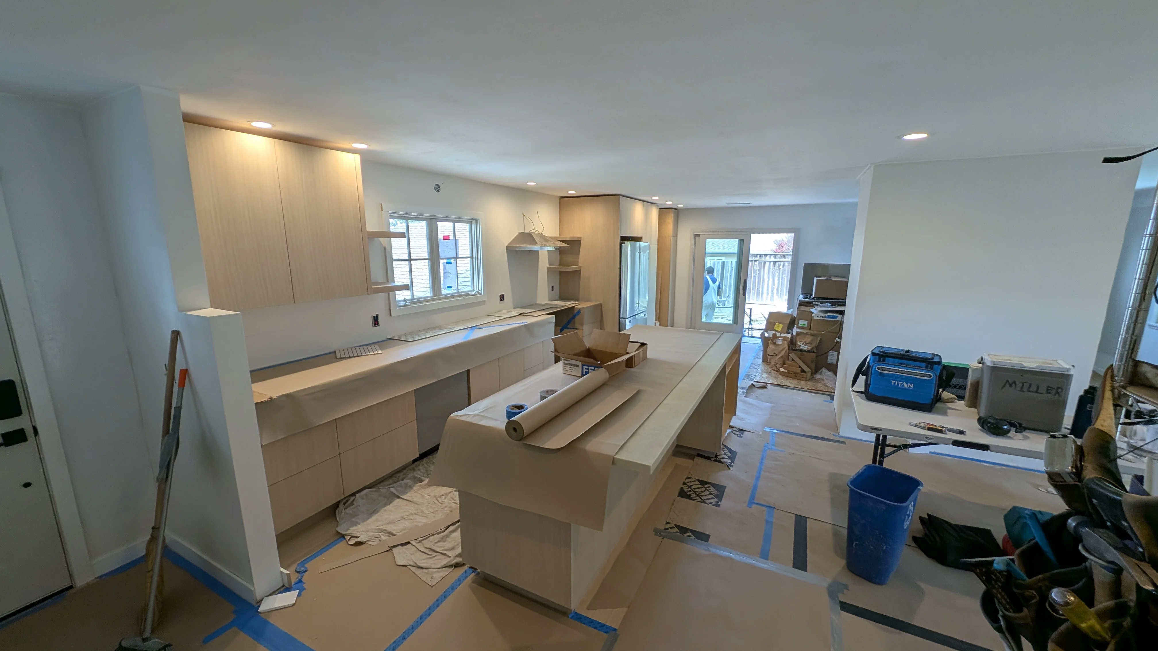 Modern kitchen under construction with light wood cabinets, island, and recessed ceiling lights